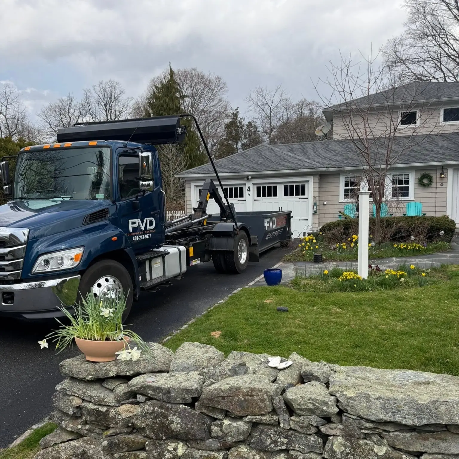 Hooklift truck collecting a loaded dumpster from a driveway in Cranston